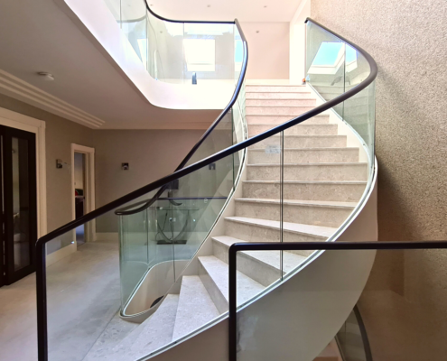 Bespoke curved staircase Private client Surrey Glass balustrade Custom-made oak handrails Modern and minimalistic Open and airy feel Unobstructed view Spacious and welcoming Low maintenance Easy to clean CNC machines French polished Warm and inviting Comfortable and safe Luxury and sophistication Focal point Unique needs Style preferences