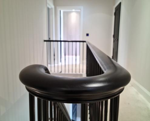 Close-up of a black-painted timber handrail wreath over black spindles on a landing