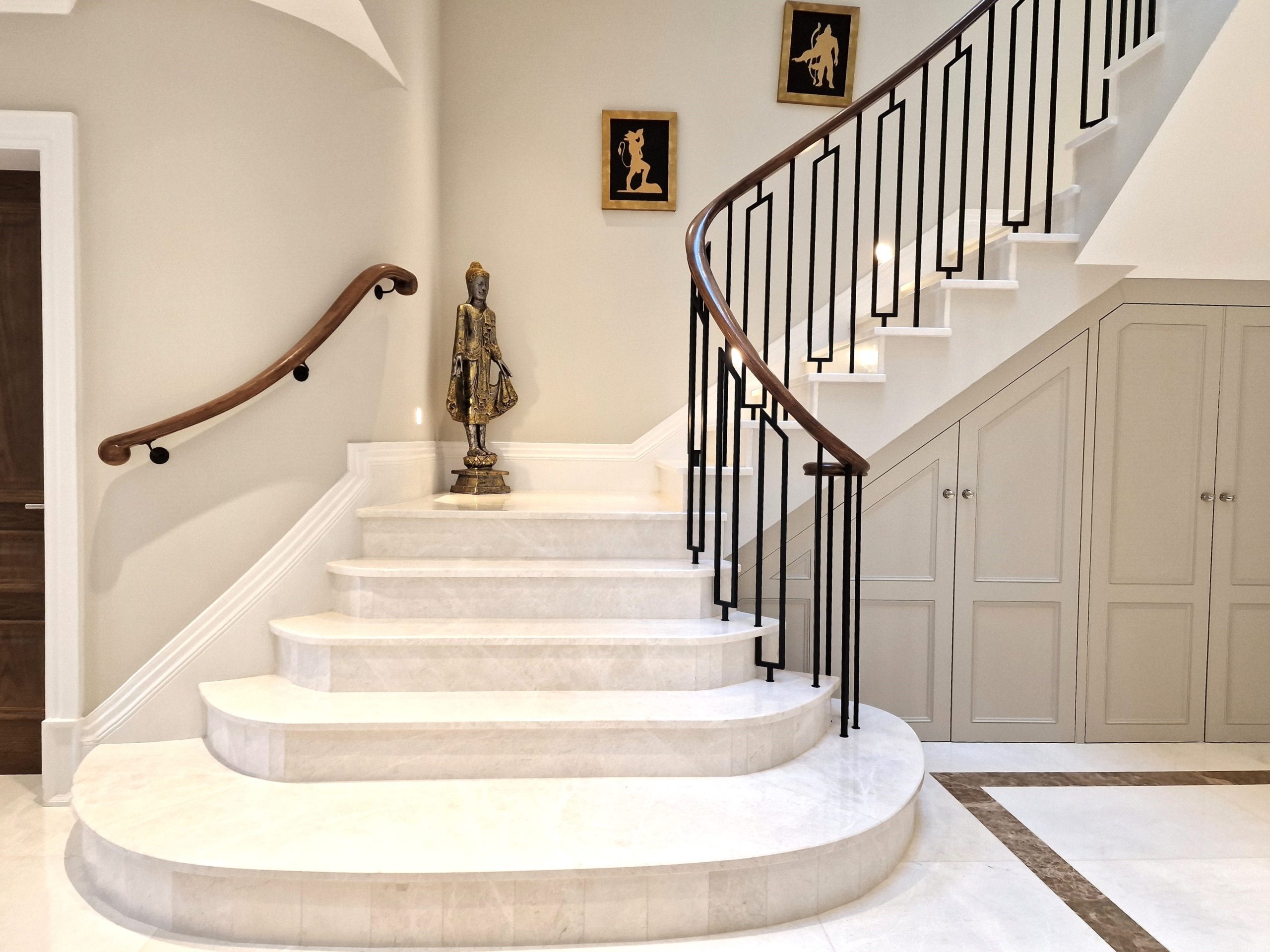 Stone staircase with brass geometric balustrade and dark timber handrail in a cream hallway