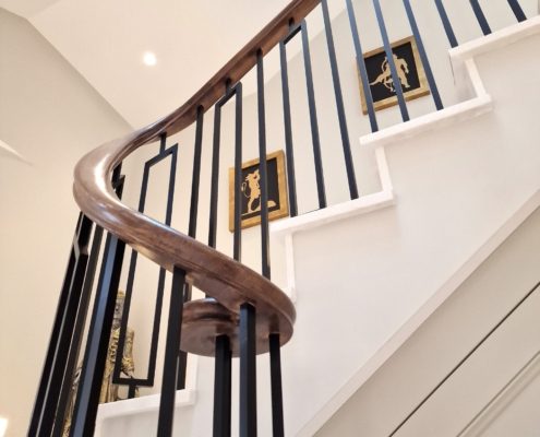 Curved timber handrail and black geometric balusters climbing a white staircase