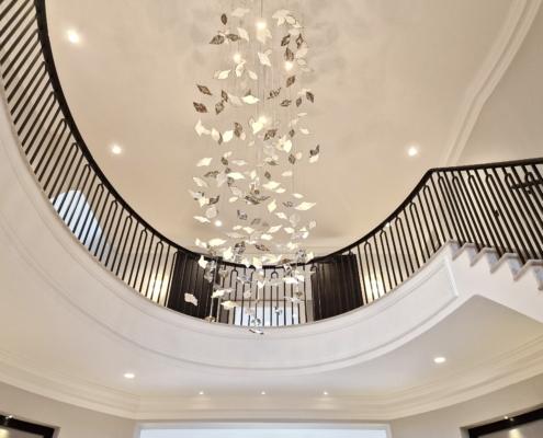 Black curved balustrade around an oval stairwell beneath a crystal chandelier
