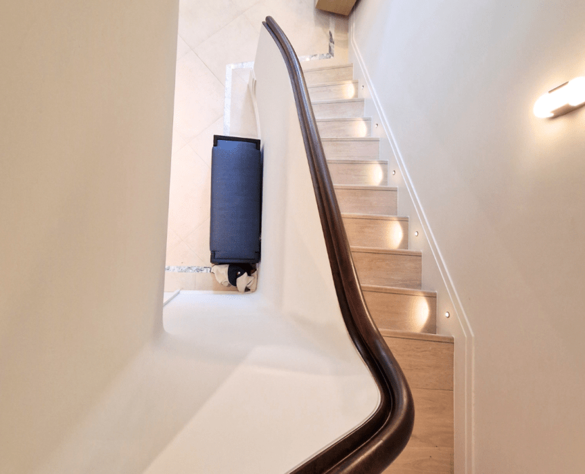 Dark timber wall-mounted handrail following a curved white staircase with lit steps