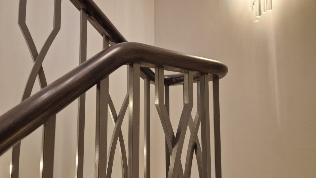 Close-up of a dark timber handrail on a bespoke metal balustrade with branch-style spindles
