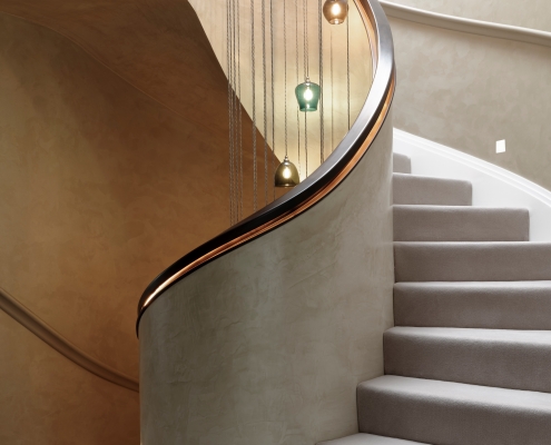 Mid section - Stone spiral staircase with Walnut helical handrails with hanging LED light fittings from ceiling