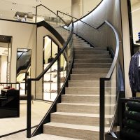 Timber profile Gloss Black handrail straight and helical sections on glass balustrade in retail store.