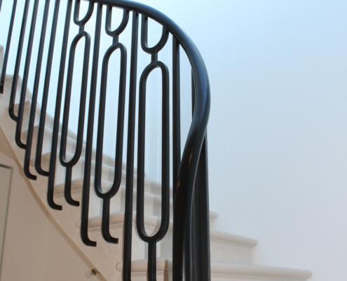 Black handrail over decorative black metal panel balustrade on a curved white staircase