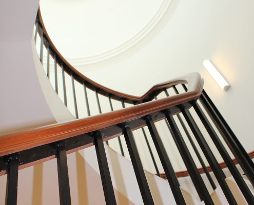 Steel core rail fixed to bespoke timber handrail on rising staircase with Black steel square spindles