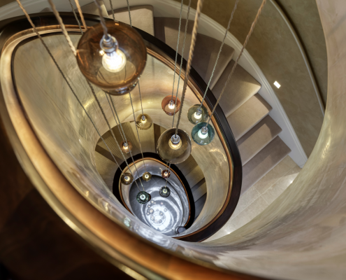 Stone spiral staircase with Walnut helical handrails with hanging LED light fittings from ceiling