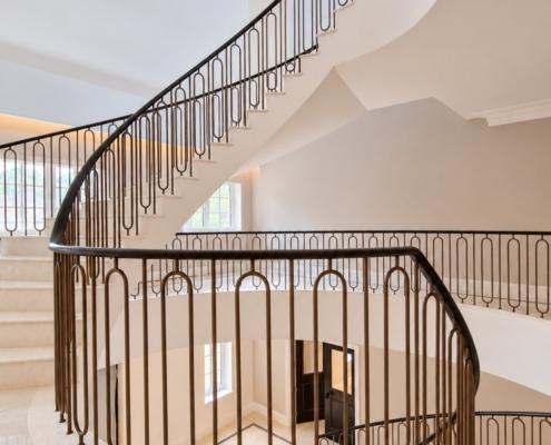 Continuous curved oak handrail following the helical stair with bronze hoop balustrade