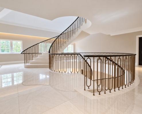 Curved stone staircase and landing balustrade with bronze painted hoop spindles and dark oak handrail