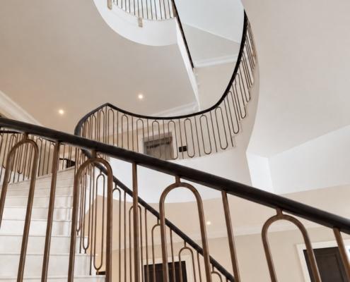 View up through the stairwell showing curved oak handrail and bronze balustrade