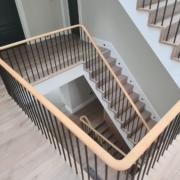 Looking down a four-storey staircase with continuous oak handrail and black steel spindles, Surrey