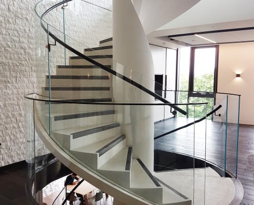 Spiral staircase with glass balustrade and Black timber helical rising handrails